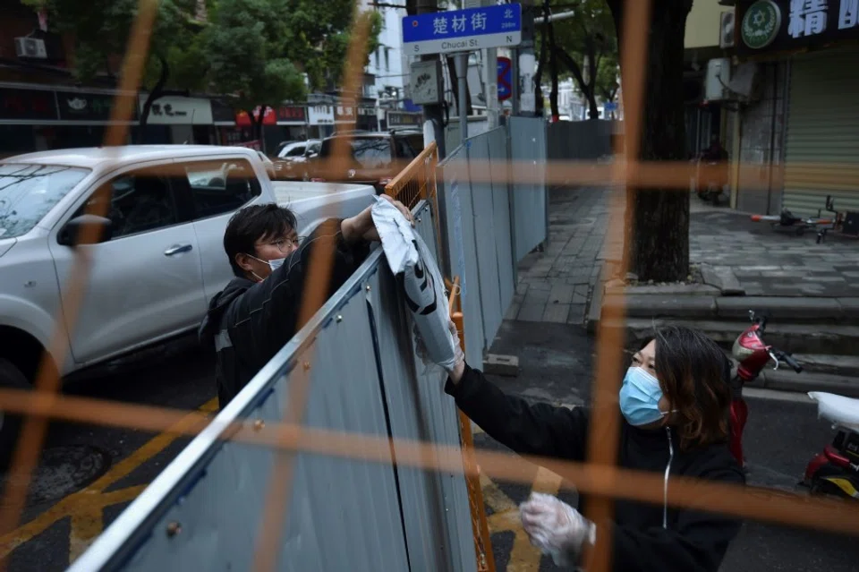 A delivery rider handing a package to a resident over a wall closing off a street in Wuhan. (STR/AFP)