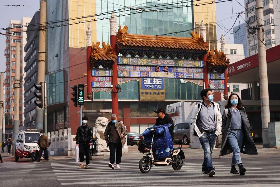 People wearing face masks cross a street in Beijing, China, on 25 October 2021. (Thomas Peter/Reuters)
