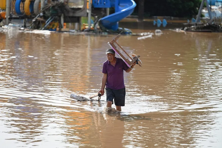 A resident carrying a table walks through a flooded area after heavy rains at Taishitun village in Miyun district, on the outskirts of Beijing on 28 July 2025.