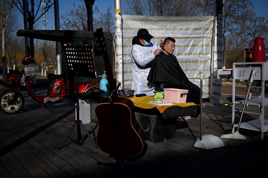 A barber cuts a man's hair along a road in Beijing, China, on 7 December 2021. (Wang Zhao/AFP)