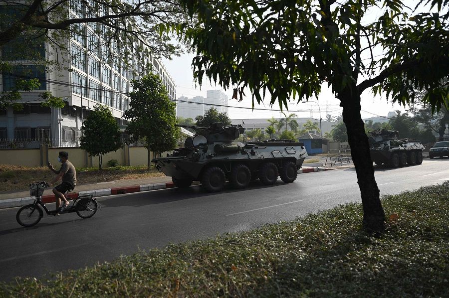 A man (left) he rides past military vehicles parked along a street in downtown Yangon on 15 February 2021, the morning after Myanmar's military cut the nation's internet and deployed extra troops around the country. (Ye Aung Thu/AFP)