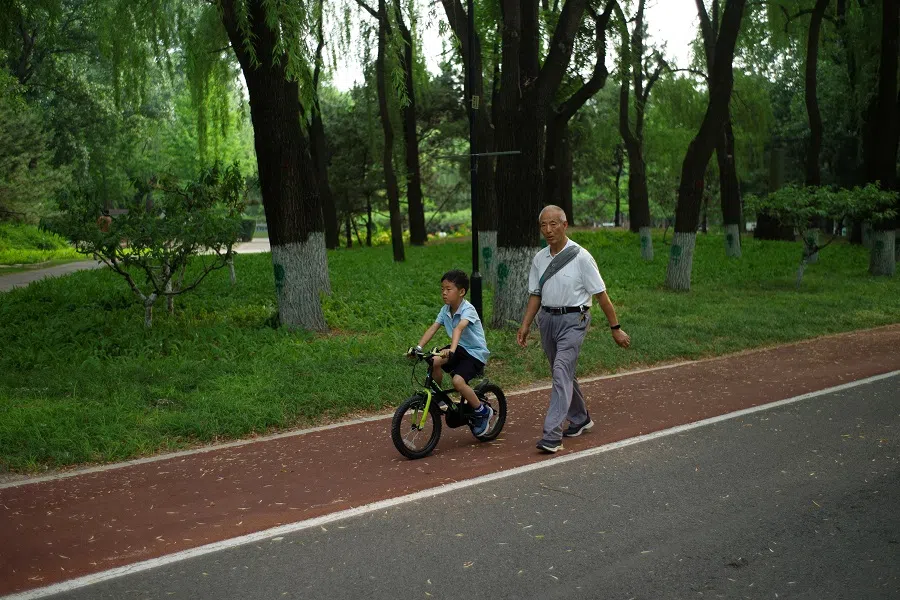 An elderly person walks next to a child at a park in Beijing, China, on 22 May 2024. (Tingshu Wang/Reuters)