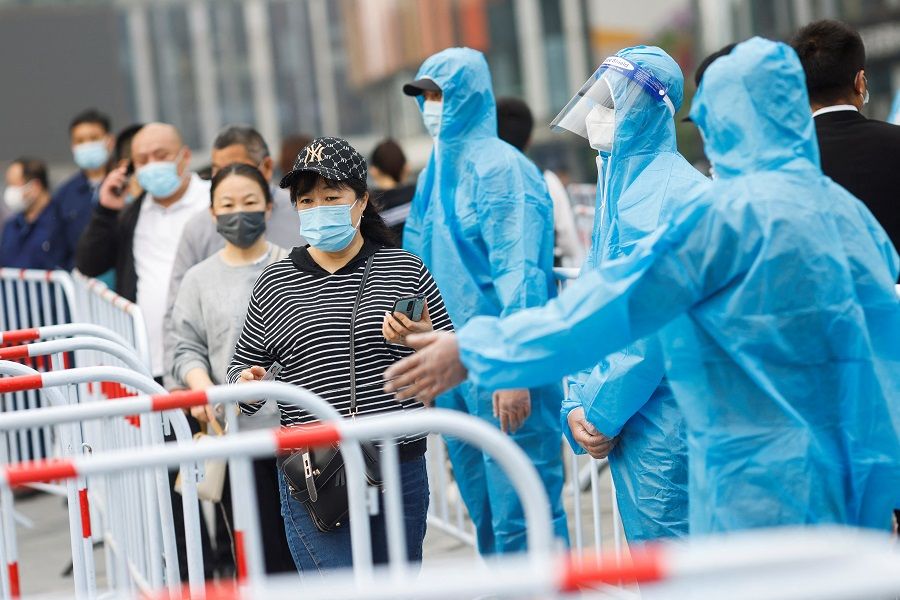People wearing face masks walk next to medical workers wearing protective suits as they line up to take nucleic acid tests at a makeshift testing site following the Covid-19 outbreak in Beijing, China, 25 April 2022. (Carlos Garcia Rawlins/Reuters)
