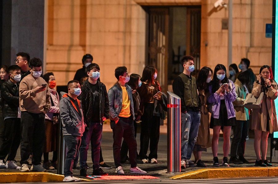 People stand at a crosswalk next to stores and shopping malls in Shanghai, China, on 24 October 2022. (Hector Retamal/AFP)