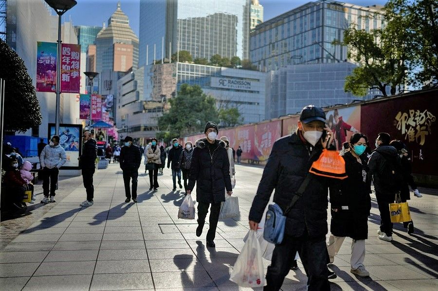 People wearing protective masks walk in a shopping district in Shanghai, China, 3 January 2023. (Aly Song/Reuters)