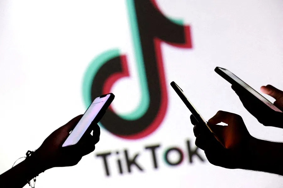 Teenagers pose for a photo while holding smartphones in front of a TikTok logo in this illustration taken on 11 September 2025.