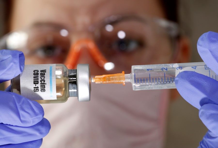 A woman holds a small bottle labeled with a "Vaccine COVID-19" sticker and a medical syringe in this illustration taken 10 April 2020. (Dado Ruvic/REUTERS)