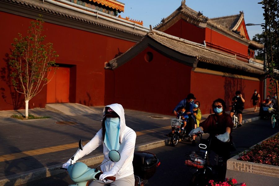 People wearing protective masks ride past Lama Temple in Beijing, China, on 19 June 2020. (Thomas Peter/Reuters)