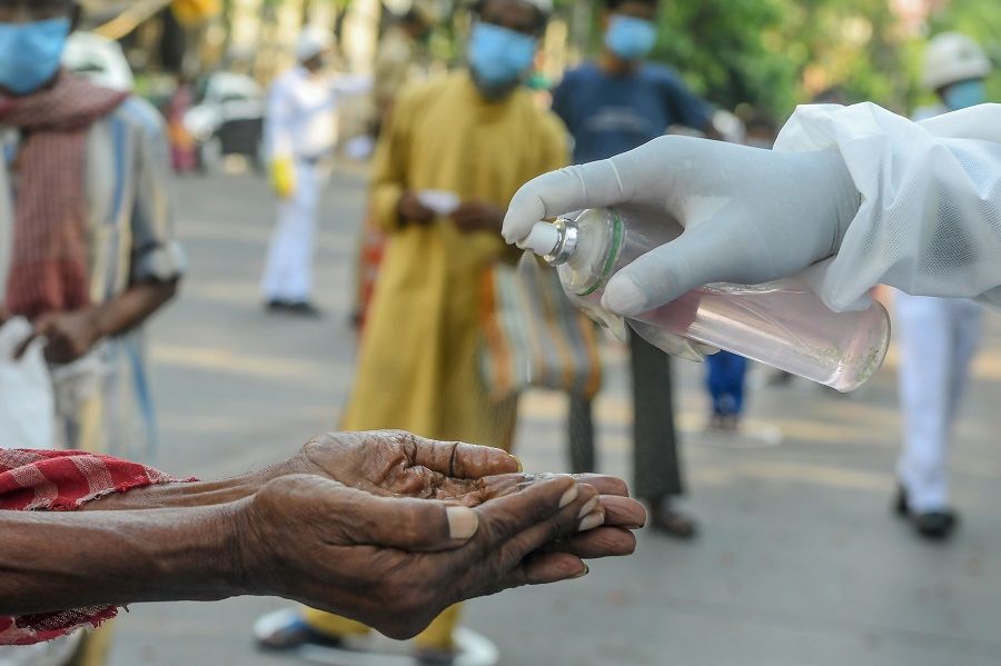 A slum dweller (left) cleans his hands with sanitiser before collecting relief material during a government-imposed nationwide lockdown as a preventive measure against the Covid-19 coronavirus, in Kolkata, India, on 30 April 2020. (Dibyangshu Sarkar/AFP)