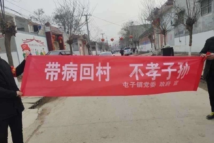 Another banner held up by villagers reads: "People who bring the virus back home are unfilial."