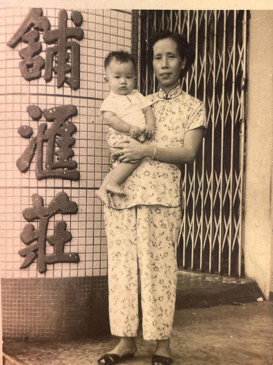 Ho Nai Chuen, second-generation successor of On Cheong Jewellery, in the arms of his mother, outside the family’s gold store. (Photo provided by On Cheong)