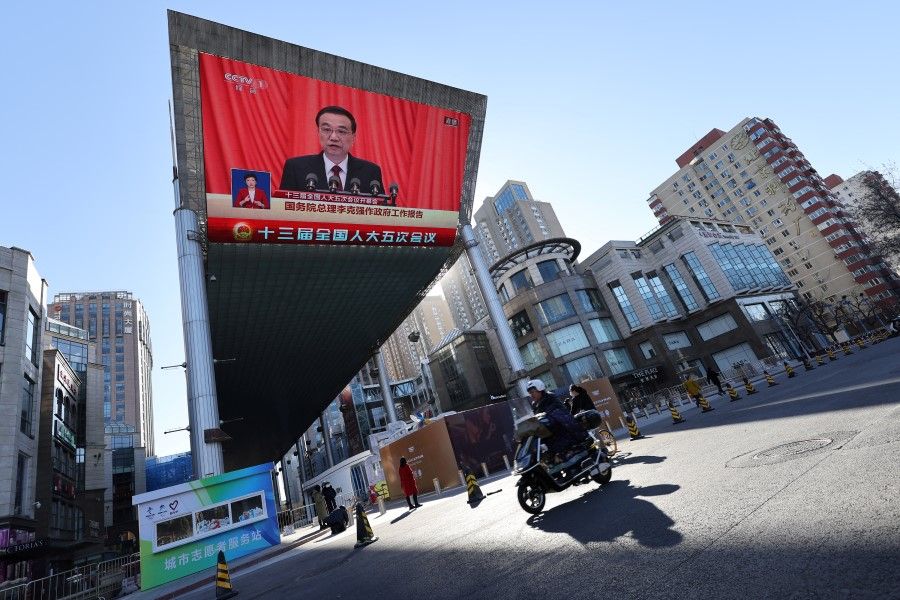 A man rides a scooter past a giant screen showing Chinese Premier Li Keqiang delivering the work report during the opening session of the National People's Congress at the Great Hall of the People, in Beijing, China, 5 March 2022. (Tingshu Wang/Reuters)