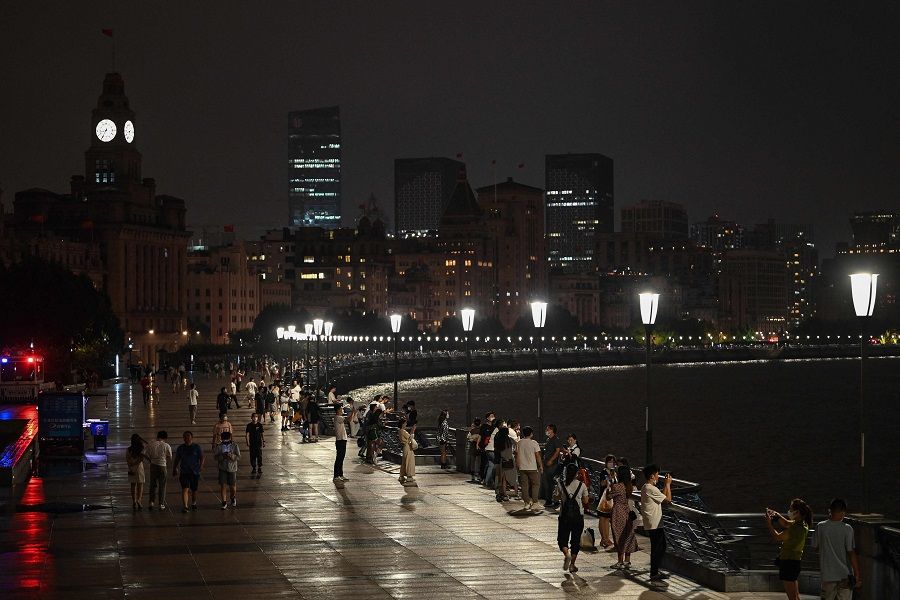 People walk along the Bund promenade as decorative lights are switched off as a measure to save energy in Shanghai, China, on 23 August 2022. (Hector Retamal/AFP)