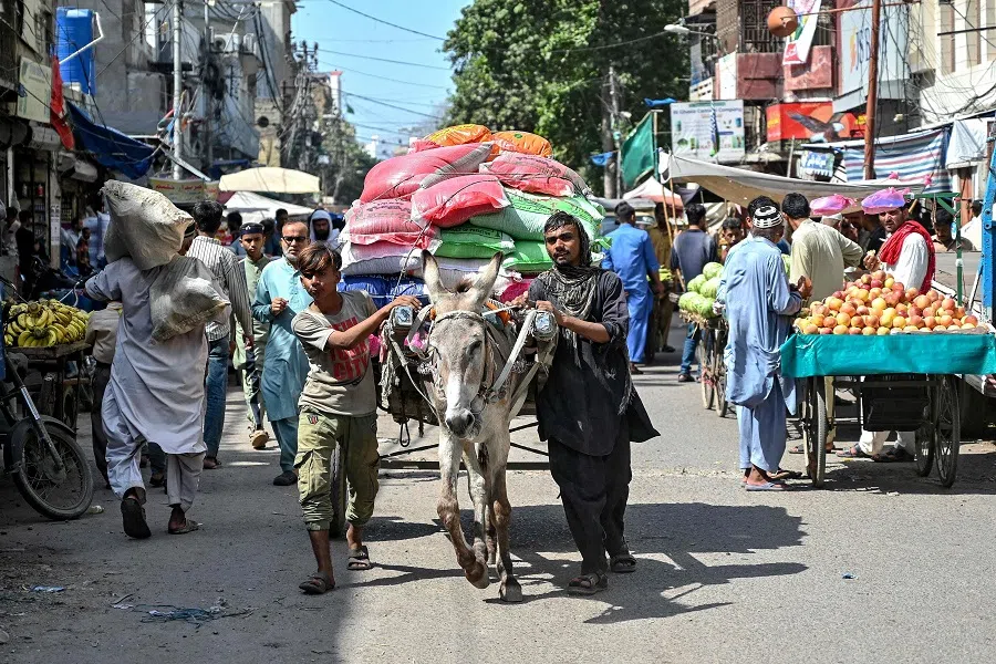 In this photograph taken on 3 October 2024, labourers, along with a loaded donkey cart, move through a street at a wholesale market in Karachi, Pakistan. (Asif Hassan/AFP)