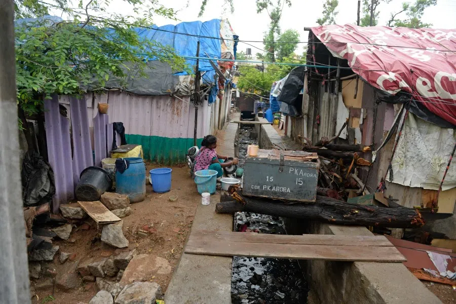 A woman washes utensils on an open drainage outside her temporary shelter at a slum area in Hyderabad, 12 June 2020. (Noah Seelam/AFP)