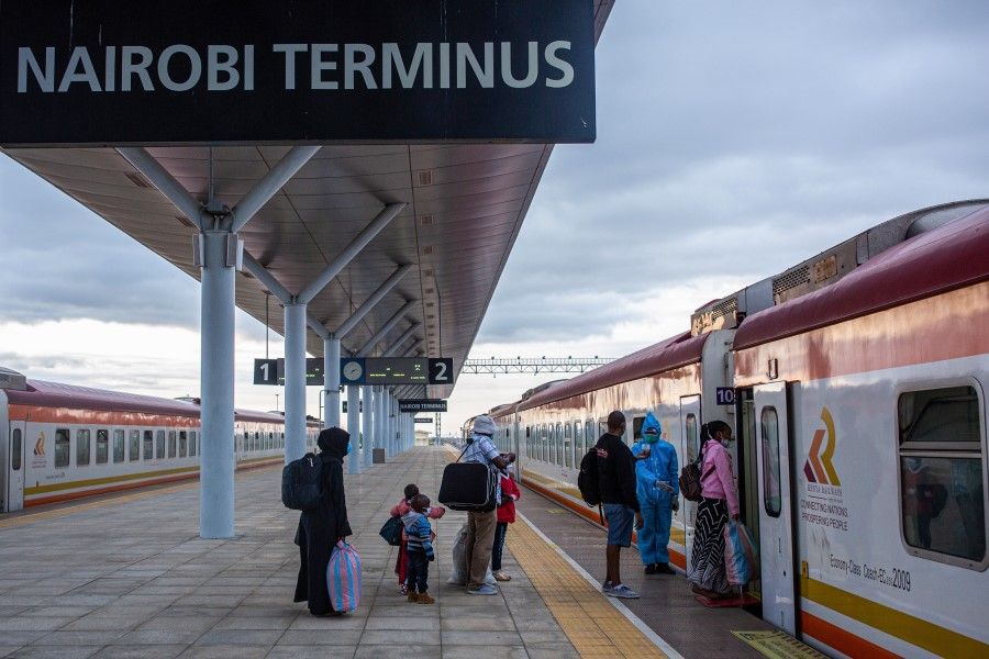 A Kenya Railways Corp. train attendant wearing personal protective equipment (PPE) assists passengers to board a train in Nairobi, 18 August 2020. The railway, funded, built and operated by Chinese agencies, started running between Kenya's port city of Mombasa to the capital, Nairobi, in 2017. (Patrick Meinhardt/Bloomberg)