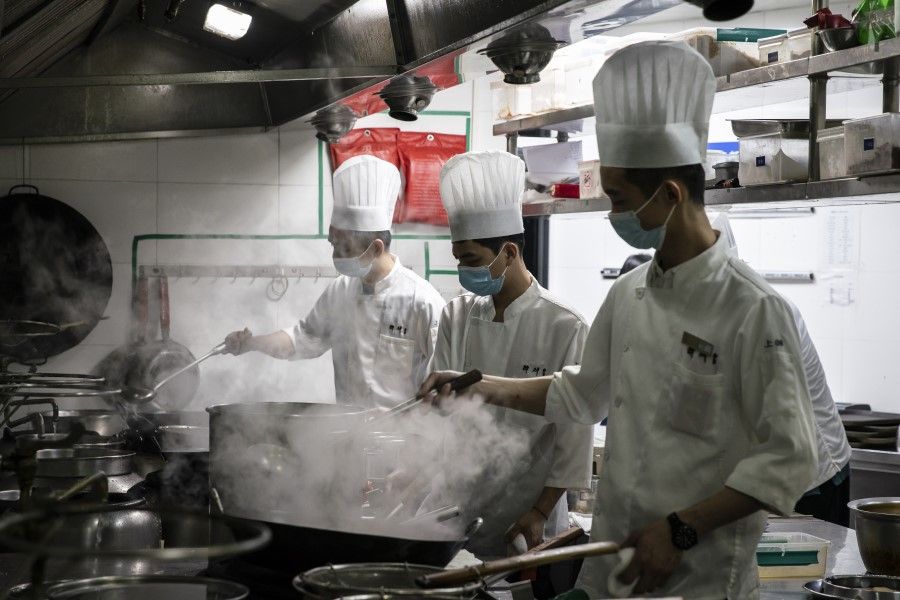 Cooks wear protective face masks as they prepare food for customers in the kitchen at a Zuihuihuang restaurant in Shanghai, China, on 12 February 2021. (Qilai Shen/Bloomberg)