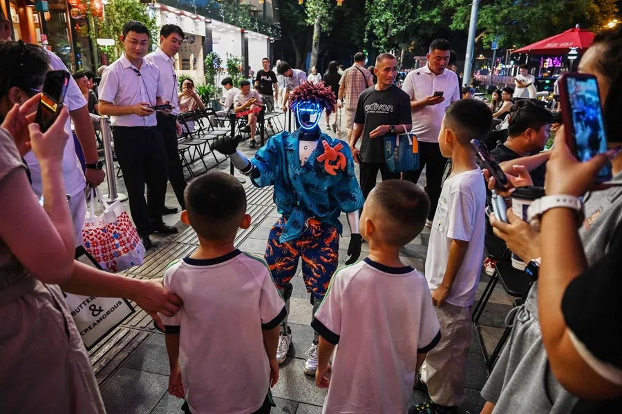 Children play with a remotely controlled humanoid robot outside a restaurant in Beijing on 28 July 2025. (Greg Baker/AFP)