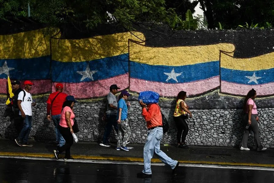 People stand in front of a mural with a Venezuelan flag in Caracas on 7 January 2026.