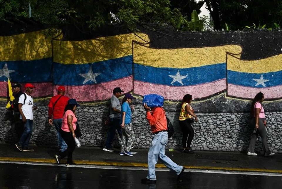 People stand in front of a mural with a Venezuelan flag in Caracas on 7 January 2026. (Ronaldo Schemidt/AFP)