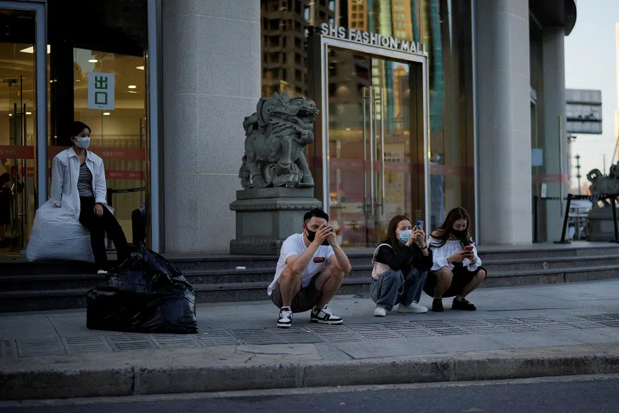 People wearing protective face masks look at their phones, outside a shopping mall in Shanghai, China, 19 September 2022. (Aly Song/Reuters)