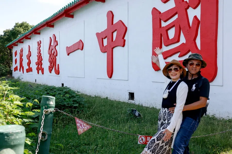 Tourists pose for photos in front of a slogan reading "Reunify China with the Three Principles of the People" referring to the political philosophy of Sun Yat-sen, founder of the Republic of China who overthrew the Qing dynasty in 1911, on Dadan Island, Kinmen, Taiwan, 18 October 2025. (Ann Wang/Reuters)