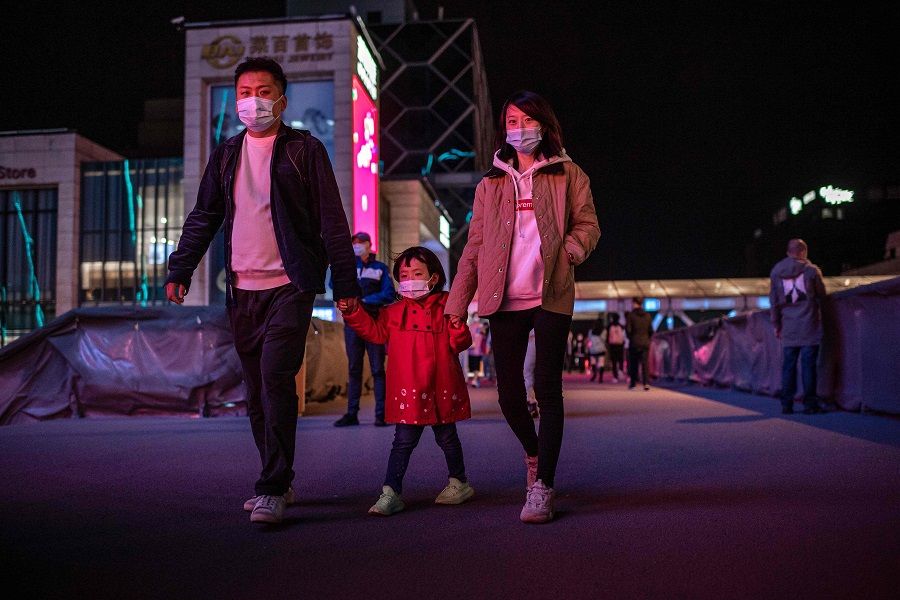 A family wearing face masks walks outside a shopping mall in Beijing on 11 October 2020. (Nicolas Asfouri/AFP)