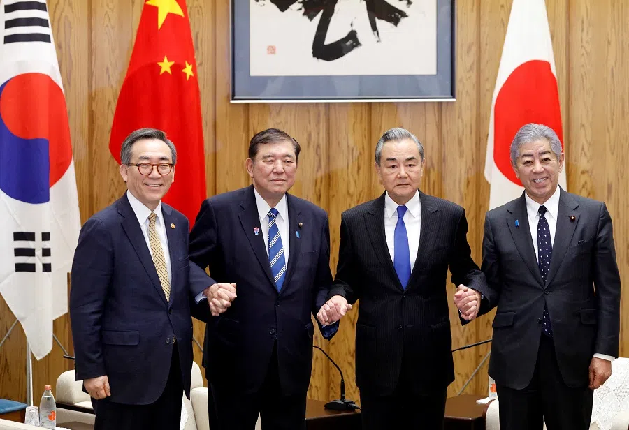 South Korean Foreign Minister Cho Tae-yul, Japanese Prime Minister Shigeru Ishiba, Chinese Foreign Minister Wang Yi and Japanese Foreign Minister Takeshi Iwaya join hands at the start of their meeting at the prime minister’s official residence in Tokyo, Japan, on 21 March 2025. (Franck Robichon/Reuters)