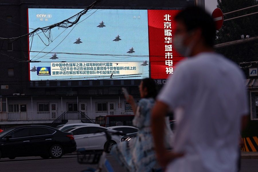 Pedestrians wait at an intersection near a screen showing footage of Chinese People's Liberation Army (PLA) aircraft during an evening news programme, in Beijing, China, 2 August 2022. (Tingshu Wang/Reuters)