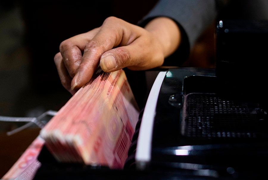 A bank employee uses a money counting machine to count out 100 RMB notes at a bank in Shanghai on 8 August 2018. While China has agreed on a debt suspension initiative, Chinese academics think that China still expects debt to be eventually repaid. (Johannes Eisele/AFP)