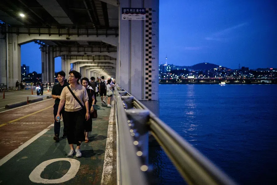 People walk across the Banpo Bridge, which stretches over the Han River in Seoul on 8 August 2025. (Anthony Wallace/AFP)
