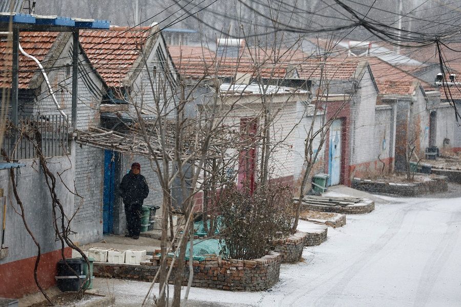 An elderly person stands outside a house amid snowfall in Beijing, China, 12 January 2023. (Tingshu Wang/Reuters)
