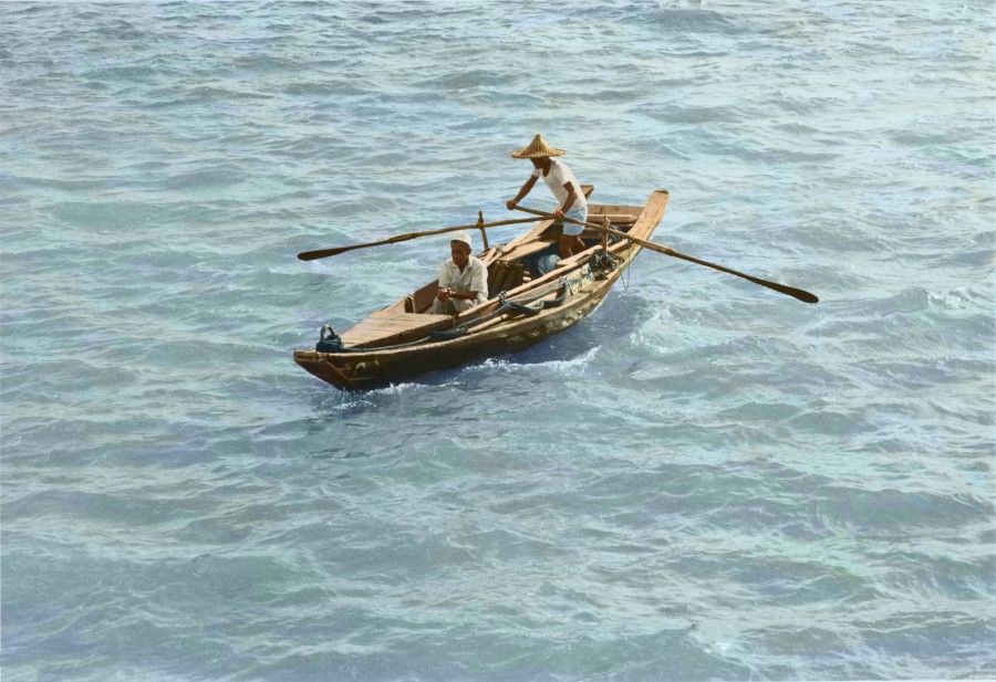 Two fishermen rowing a small traditional wooden boat in Singapore, 1950s.