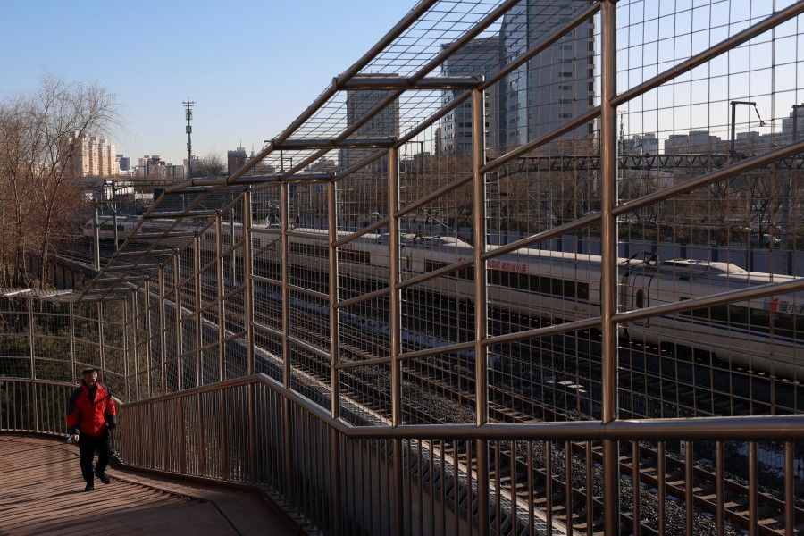 A man walks on a pedestrian bridge near a passing train in Beijing, China, on 15 January 2024. (Florence Lo/Reuters)
