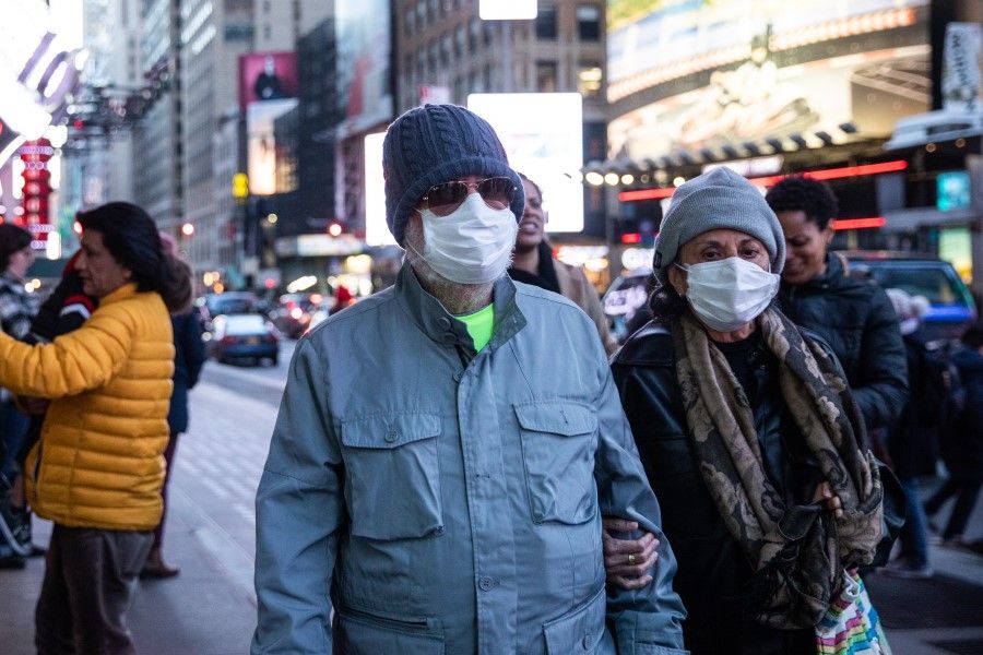 Pedestrians wear protective masks while walking in New York, 7 March 2020. The availability of testing in the US lags far behind the needs of public health workers on the front lines. (Jeenah Moon/Bloomberg)