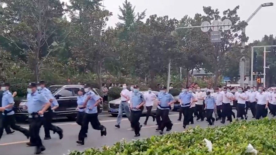 Uniformed and plain-clothed security personnel run to approach demonstrators, outside a People's Bank of China building, who are there protesting over the freezing of deposits by some rural-based banks, in Zhengzhou, Henan province, China, 10 July 2022, in this screengrab from video obtained by Reuters. (Reuters)