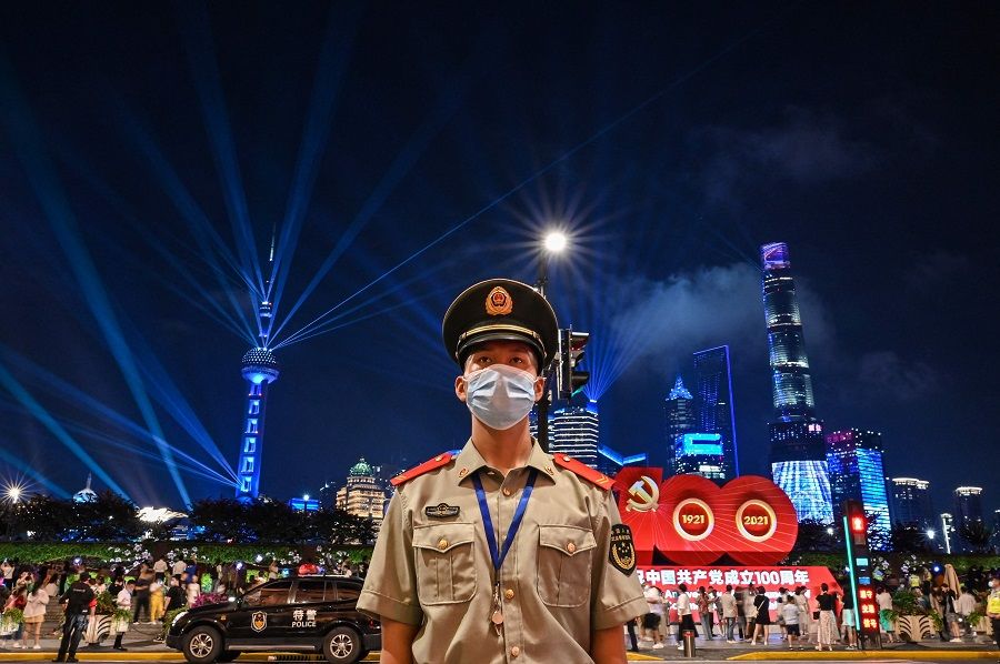 A Chinese paramilitary police stands guard while a light show is seen from the Bund in Shanghai on 30 June 2021, on the eve of the 100th anniversary of the Chinese Communist Party. (Hector Retamal/AFP)