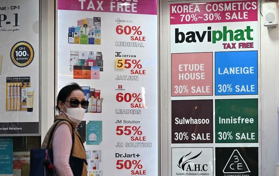 A woman walks past commercial signs at the Myeongdong shopping district in Seoul, South Korea, on 12 October 2022. (Jung Yeon-je/AFP)