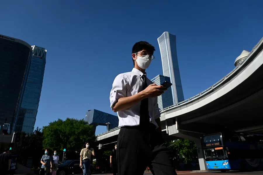 This picture taken on 6 July 2022 shows pedestrians crossing a street in Beijing's central business district, in China. (Wang Zhao/AFP)