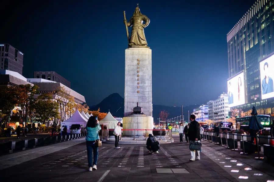 People take photos in front of the statue of Admiral Yi Sun-sin in the Gwanghwamun district of Seoul on 7 November 2025. (Anthony Wallace/AFP)