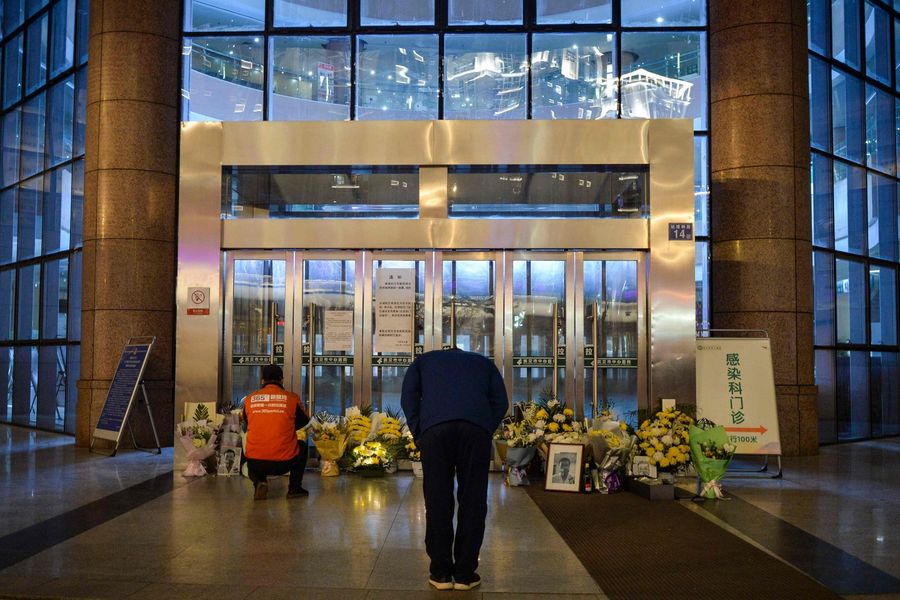 This photo taken on 7 February 2020 shows a man bowing in front of flowers and a photo of the late ophthalmologist Li Wenliang outside the Houhu Branch of Wuhan Central Hospital. (STR/AFP)