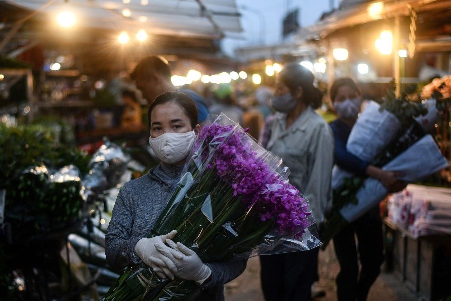 A woman wearing a face mask amid concerns over the spread of the Covid-19 coronavirus carries flowers at the Quang Ba flower market in Hanoi at dawn on 11 May 2020. (Manan Vatsyayana/AFP)