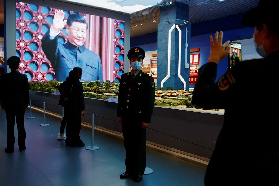 A member of the Chinese People's Liberation Army (PLA) poses for pictures in front of models of military equipment and a giant screen displaying Chinese President Xi Jinping, at an exhibition at the Military Museum of the Chinese People's Revolution in Beijing, China, 8 October 2022. (Florence Lo/Reuters)