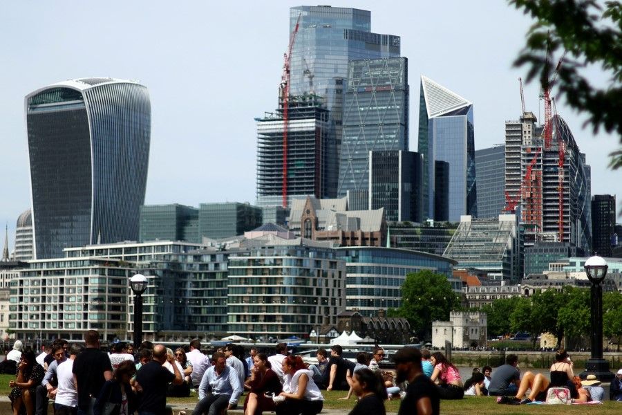People enjoy warm weather in front of the city of London financial district in London, Britain, 18 May 2022. (Hannah McKay/Reuters)