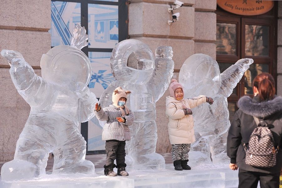 Children play with an ice sculpture of three astronauts in Harbin, Heilongjiang province, China, on 28 December 2021. (AFP)