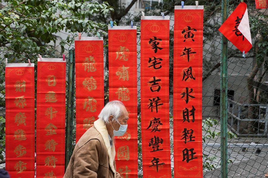 A man wearing a face mask walks past Chinese calligraphy with words of blessing on red paper for sale on Chinese New Year's Eve, in Hong Kong, China, 31 January 2022. (Lam Yik/Reuters)