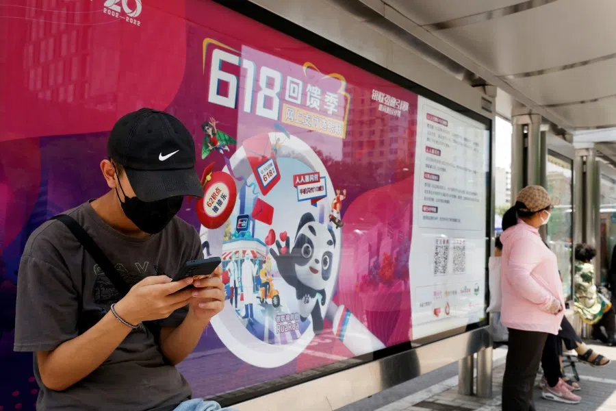 A man uses his mobile phone in front of a Unionpay advertisement for the "618" shopping festival displayed at a bus stop, in Beijing, China, 14 June 2022. (Carlos Garcia Rawlins/Reuters)