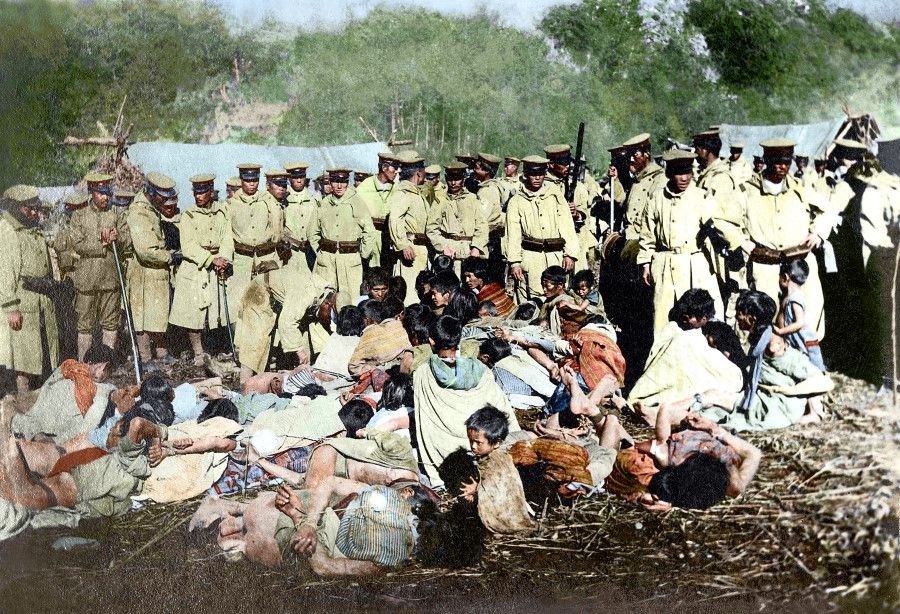 Truku people captured and gathered by Japanese troops during the Truku War of 1914. Adult men are tied up and pressed to the ground, while the young people shrink in a group. A frightened, confused three-year-old boy sits beside his father, tied up on the ground.