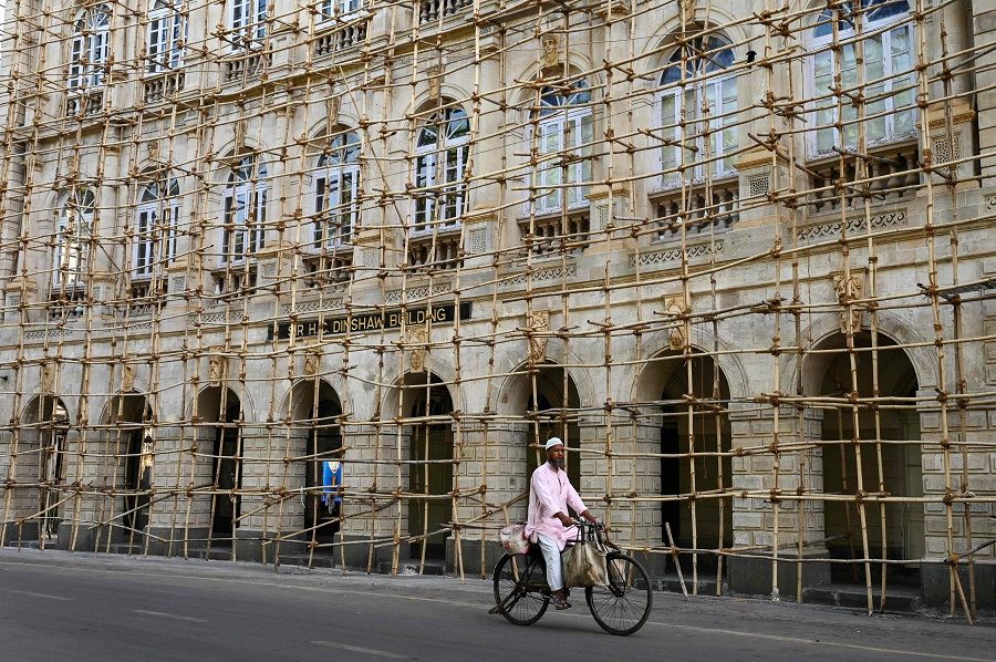 A man rides a bicycle past a building with bamboo scaffolding under renovation works in Mumbai, India, on 25 March 2023. (Punit Paranjpe/AFP)