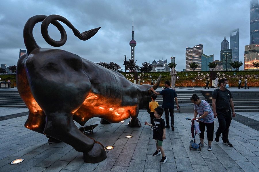 This photo taken on 9 June 2021 shows people standing next to the Bund Bull sculpture in Shanghai, China. (Hector Retamal/AFP)
